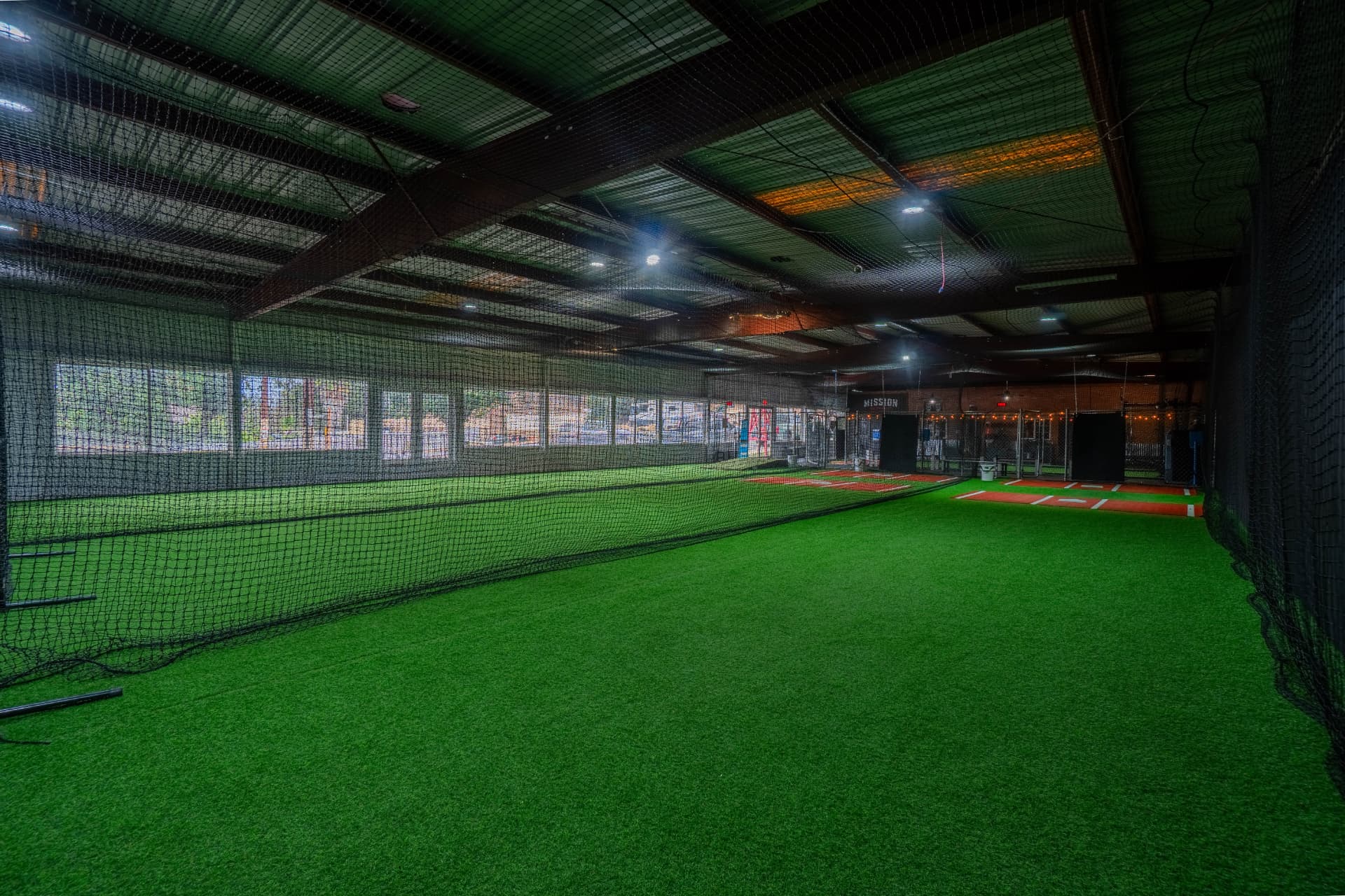 Indoor turf training field with netted batting cage lanes at Mission Athletics Club