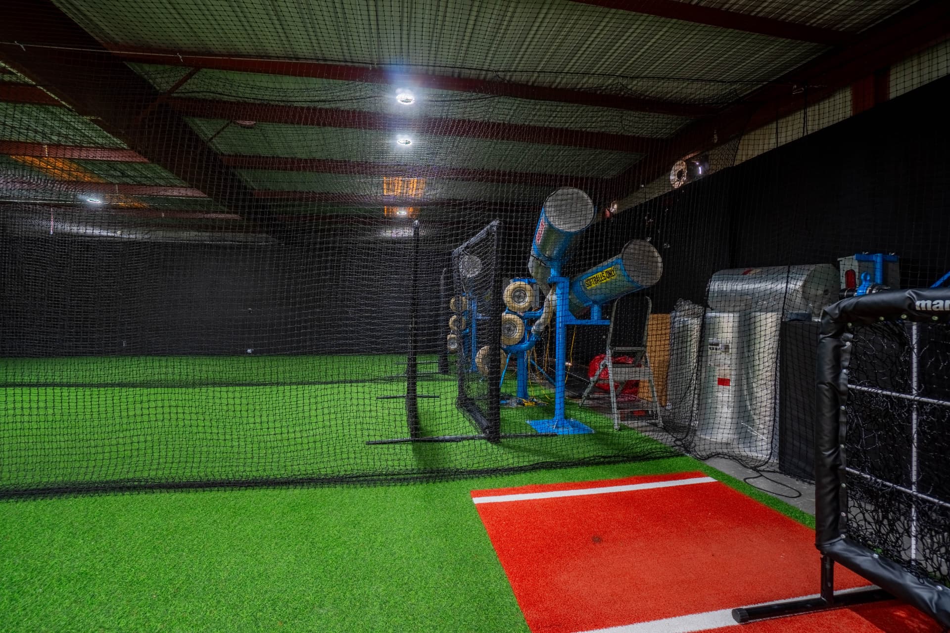 Pitching machines set up inside a netted batting cage